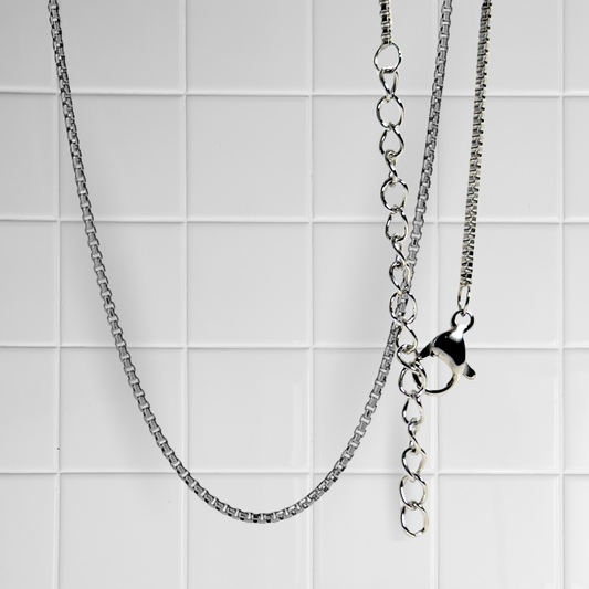 Silberne Box Chain Kette mit Verlängerungskette und Verschluss vor weißem Kachel-Hintergrund
