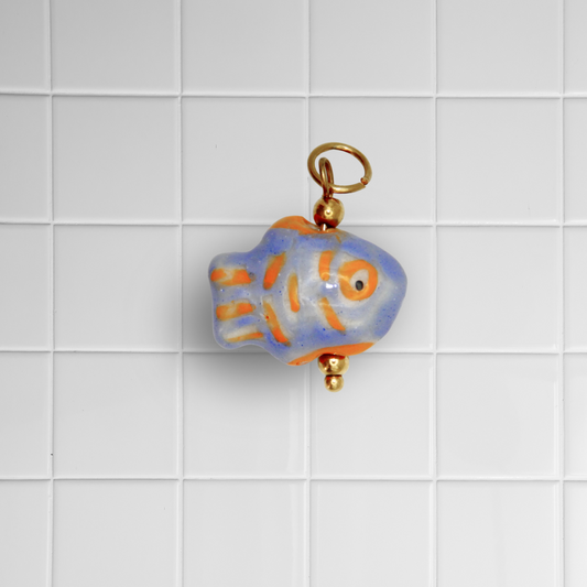 Blau-orangefarbener Keramikfisch-Anhänger mit goldener Öse auf weißem Kachel-Hintergrund