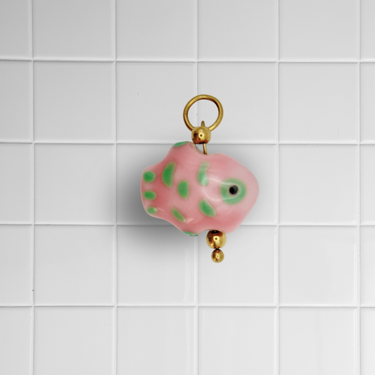 Rosa-grüner Glasfisch-Anhänger mit goldener Öse auf weißem Kachel-Hintergrund