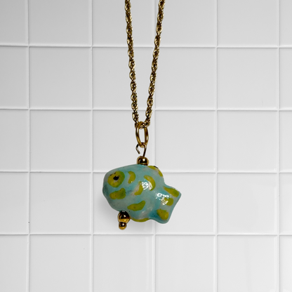 Keramikfisch-Anhänger an goldener gedrehter Kette vor weißem Kachel-Hintergrund