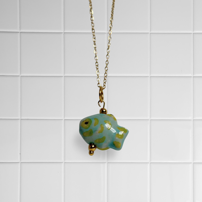 Goldene Link Chain Kette mit grün-gelben Keramikfisch-Anhänger vor weißem Kachel-Hintergrund