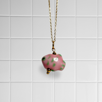 Goldene Link Chain Kette mit rosa-gruenem Keramikfisch-Anhänger vor weißem Kachel-Hintergrund