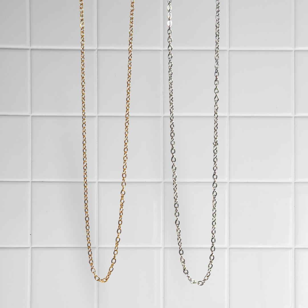 Zwei Link Chain Ketten in Gold und Silber vor weißem Kachel-Hintergrund