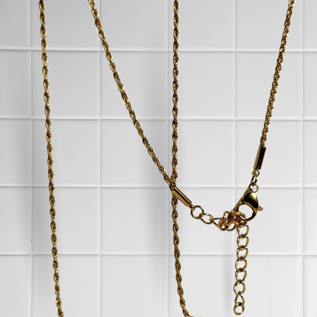 Gedrehte Rope-Kette in Gold vor weißem Kachel-Hintergrund