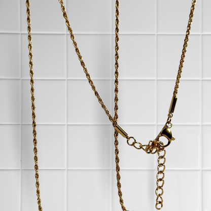 Gedrehte Rope-Kette in Gold vor weißem Kachel-Hintergrund