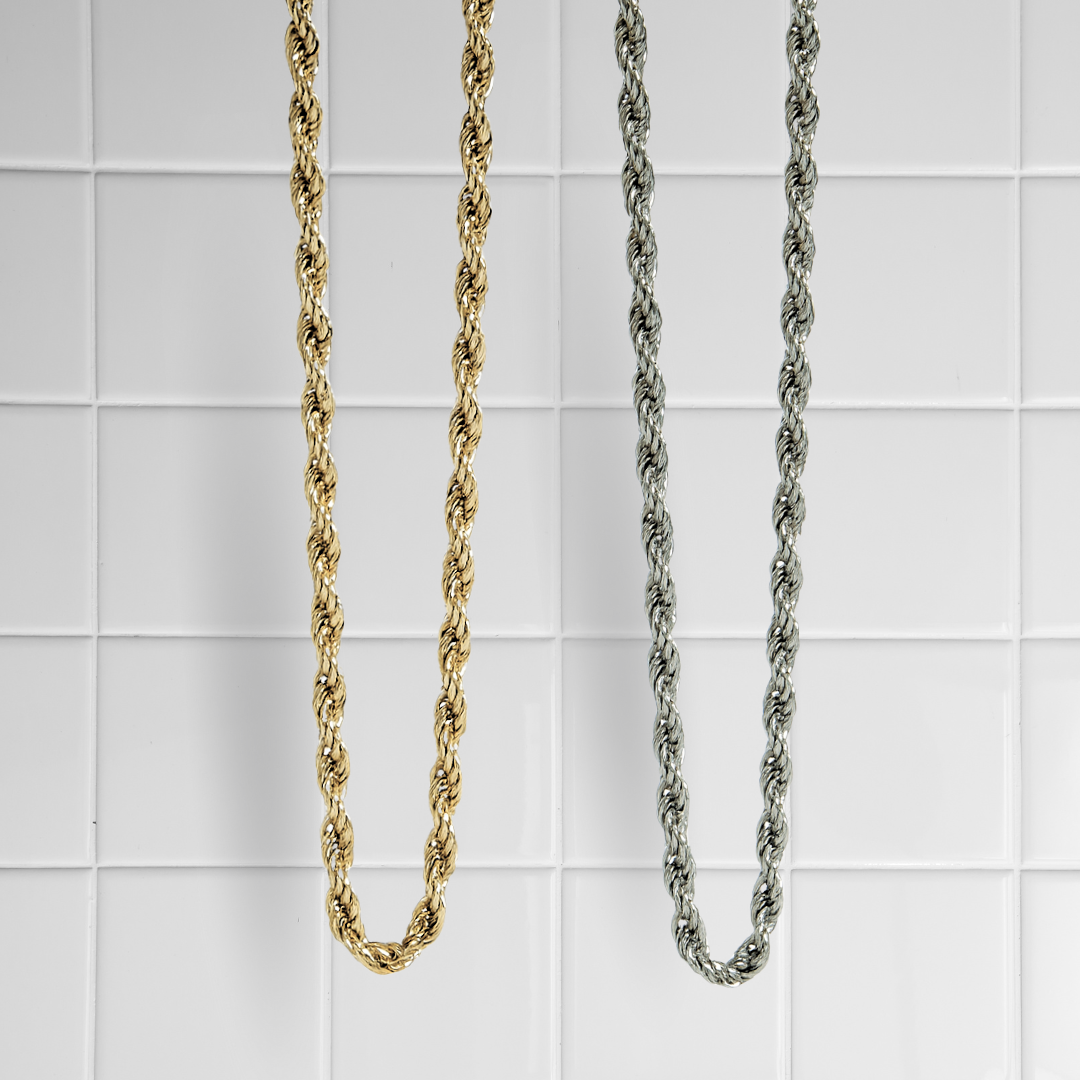 Zwei gedrehte Rope-Ketten in Gold und Silber vor weißem Kachel-Hintergrund