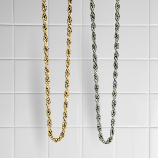 Zwei gedrehte Rope-Ketten in Gold und Silber vor weißem Kachel-Hintergrund
