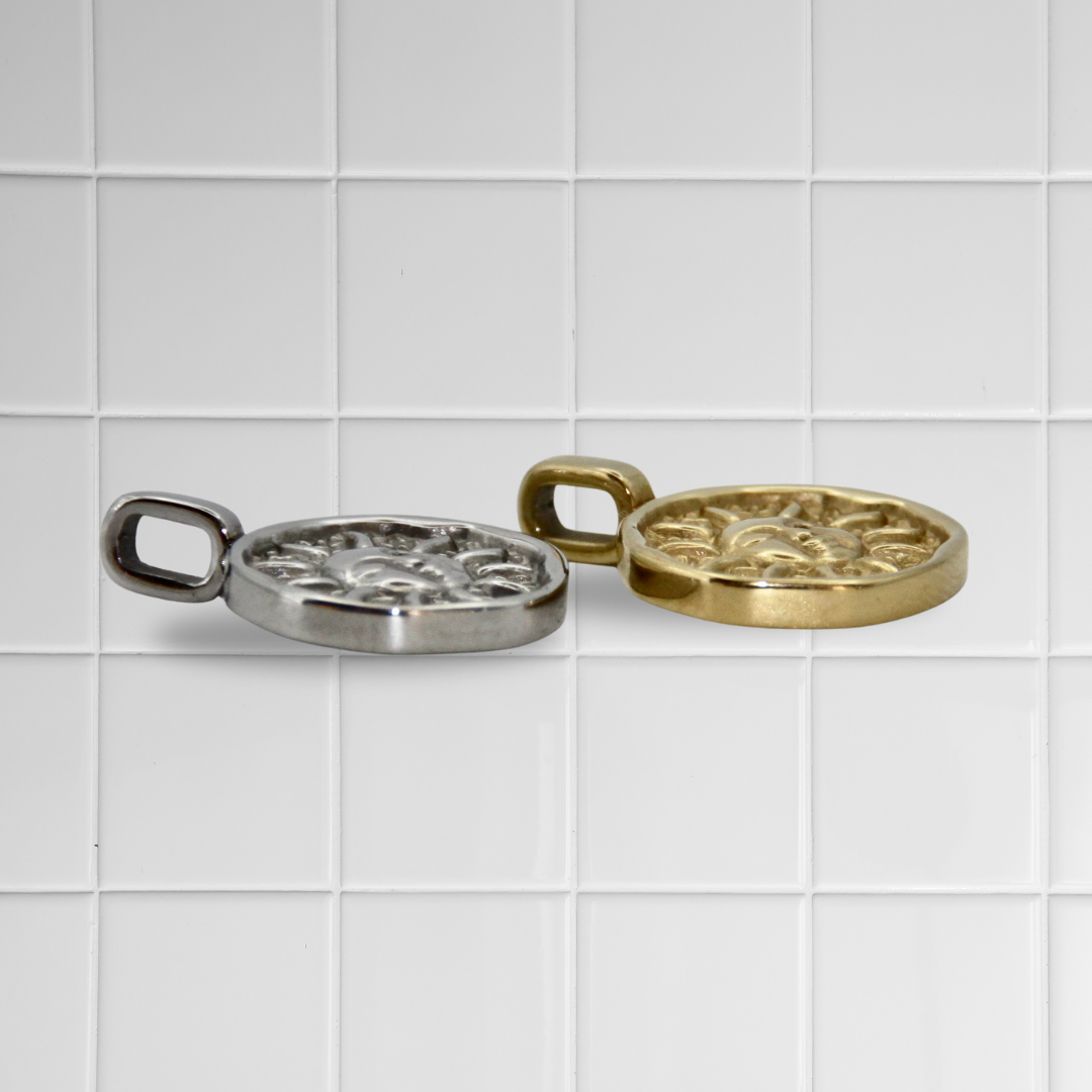 Zwei Sonnen-Anhänger aus Edelstahl in Silber und Gold auf weißem Kachel-Hintergrund