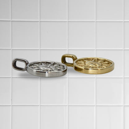 Zwei Sonnen-Anhänger aus Edelstahl in Silber und Gold auf weißem Kachel-Hintergrund