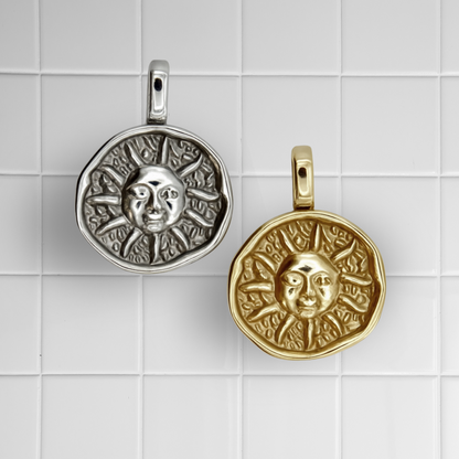 Zwei Sonnen-Anhänger aus Edelstahl in Silber und Gold auf weißem Kachel-Hintergrund